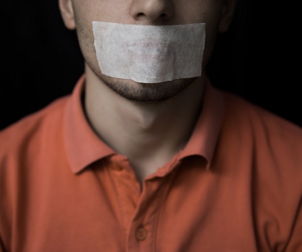 Man in orange shirt with tape over his mouth