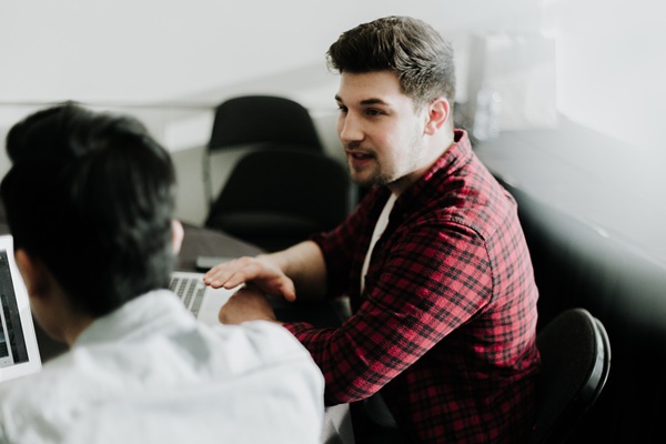 Men wearing casual clothing chatting at a table in front of laptops