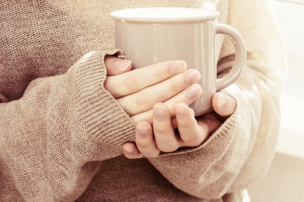 Person in beige jumper holding a beige cup of coffee