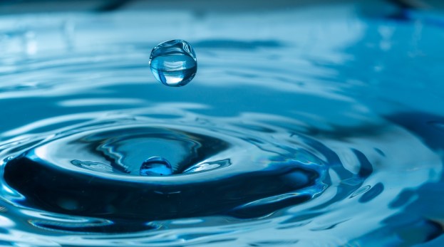 Close-up of droplet of water falling into puddle creating ripples