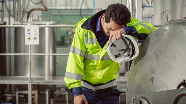 Tired fatigued worker wearing PPE next to machinery