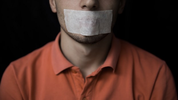 Man in orange shirt with tape over his mouth