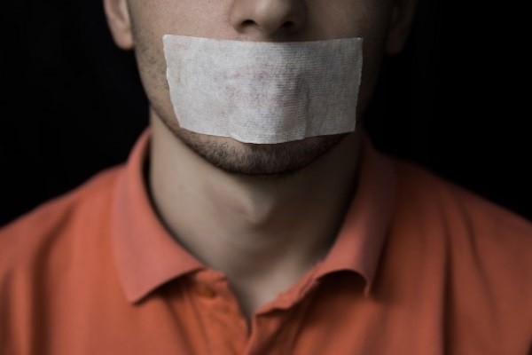 Man in orange shirt with tape over his mouth