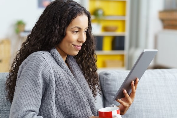 Woman with a coffee in one hand reading from a tablet in the other