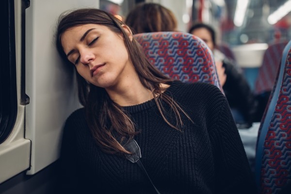 Young woman with closed eyes resting against a wall on public transport.