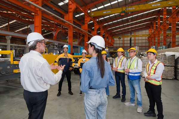 Group of people in hard hats listening to a man in a work setting.