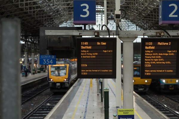 Train station platform with departure boards showing train information and arriving trains.