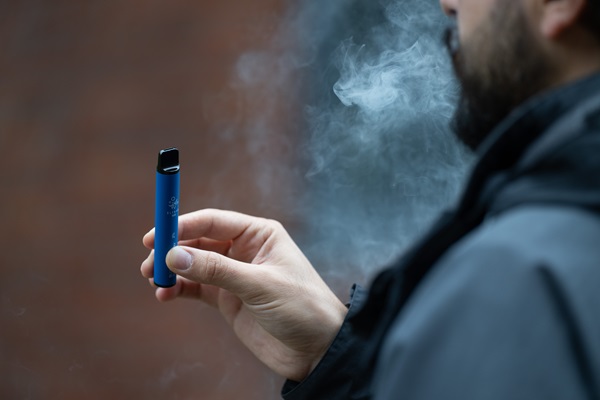Hand holding a blue e-cigarette with white vapor being exhaled.