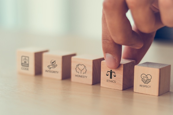 Integrity, honesty, ethics and respect representing business culture on wooden blocks, with a hand holding the block representing ethics.