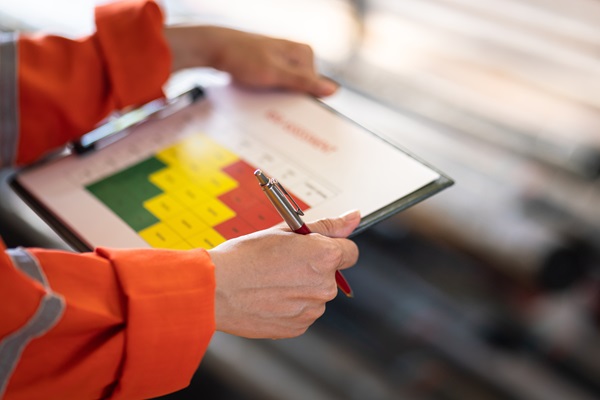 Worker in PPE holding a pen and a clipboard showing a risk assessment matrix