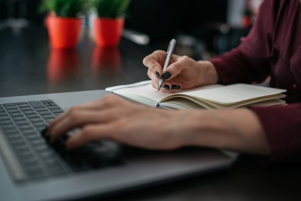 Woman writing on a notepad with her laptop open in front