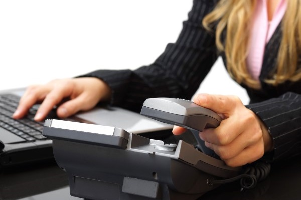 Woman putting down a phone handset with her other hand on a keyboard