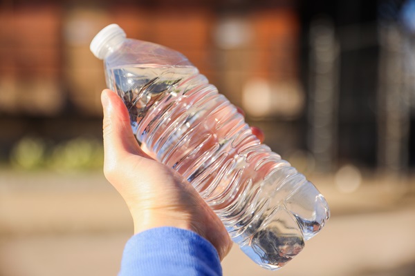 A hand holding a clear plastic bottle of water outdoors on a sunny day.
