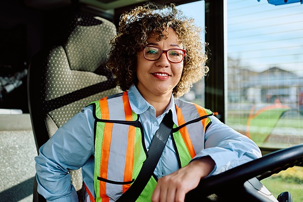 female bus driver smiling at the camera with her arm resting on the steering wheel